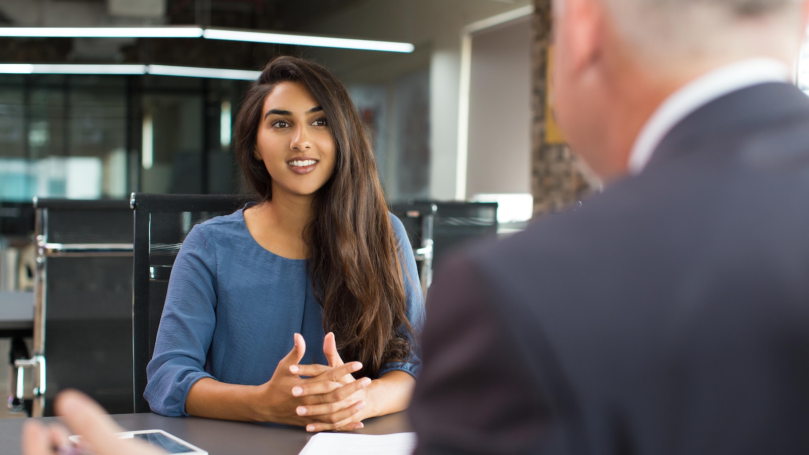 Une jeune femme sourit à un homme assise devant elle lors d'une réunion de travail.