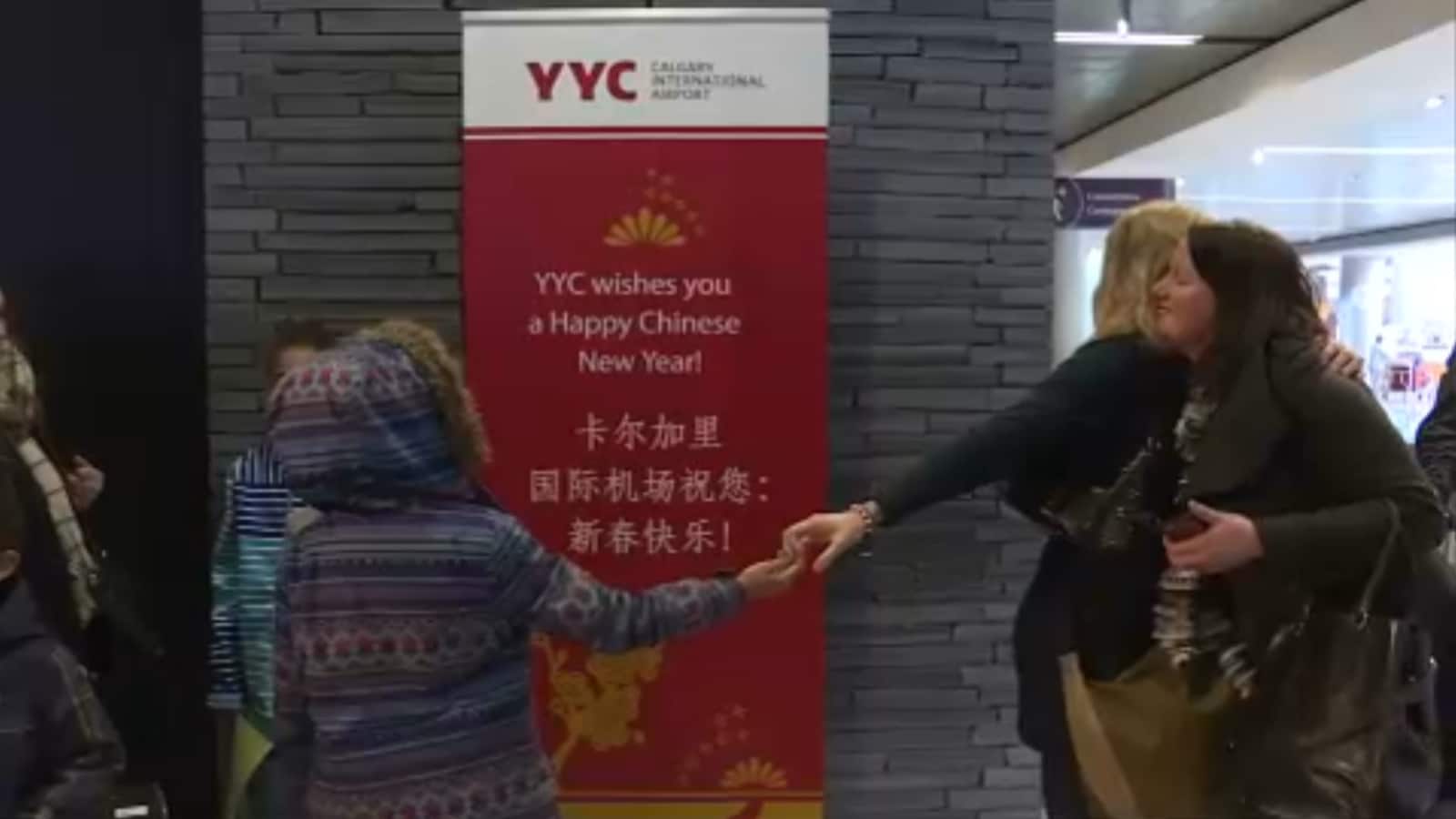 Deux femmes s'enlacent dans l'espace réservé aux arrivées à l'aéroport de Calgary.