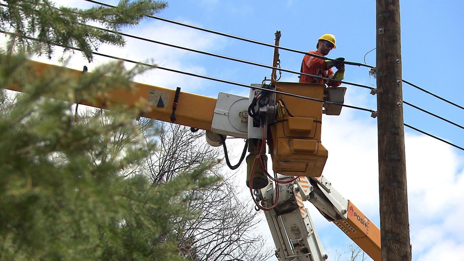Un homme, dans une petite cabine d'une grue d'Hydro-Québec jaune, répare des fils électriques.