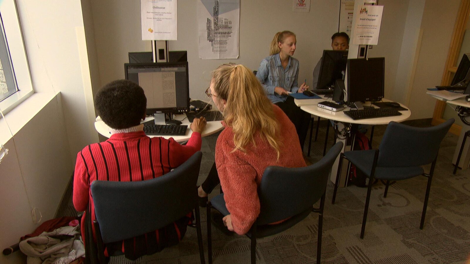 Dans le local, deux tutrices installées devant des ordinateurs aident chacune une étudiante avec leurs travaux.