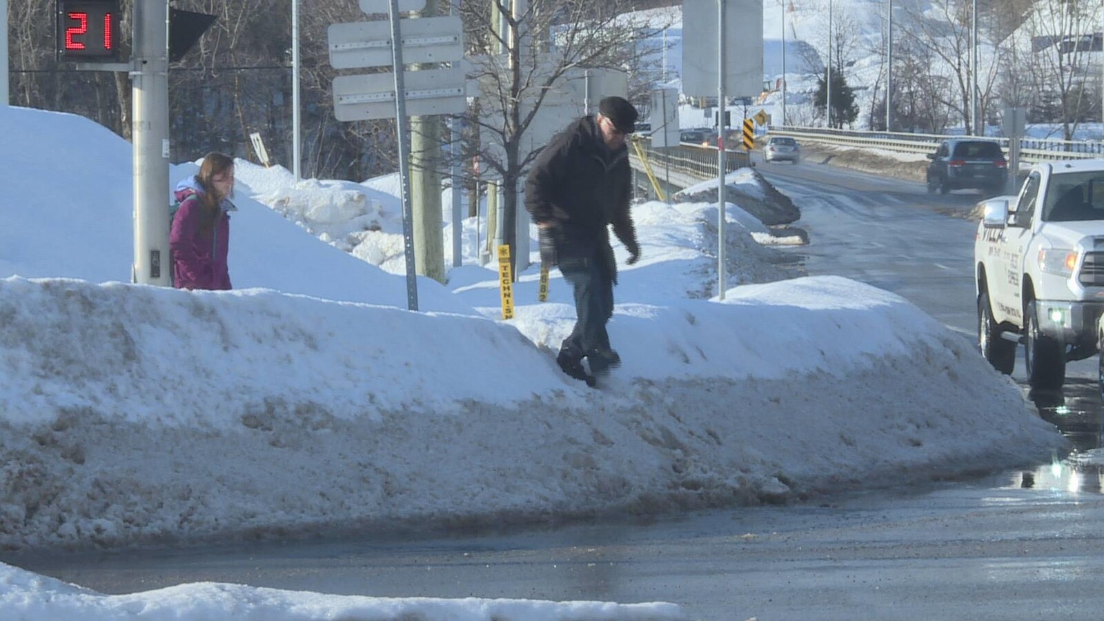 Un homme tente de franchir un banc de neige pendant que des voitures sont à proximité.
