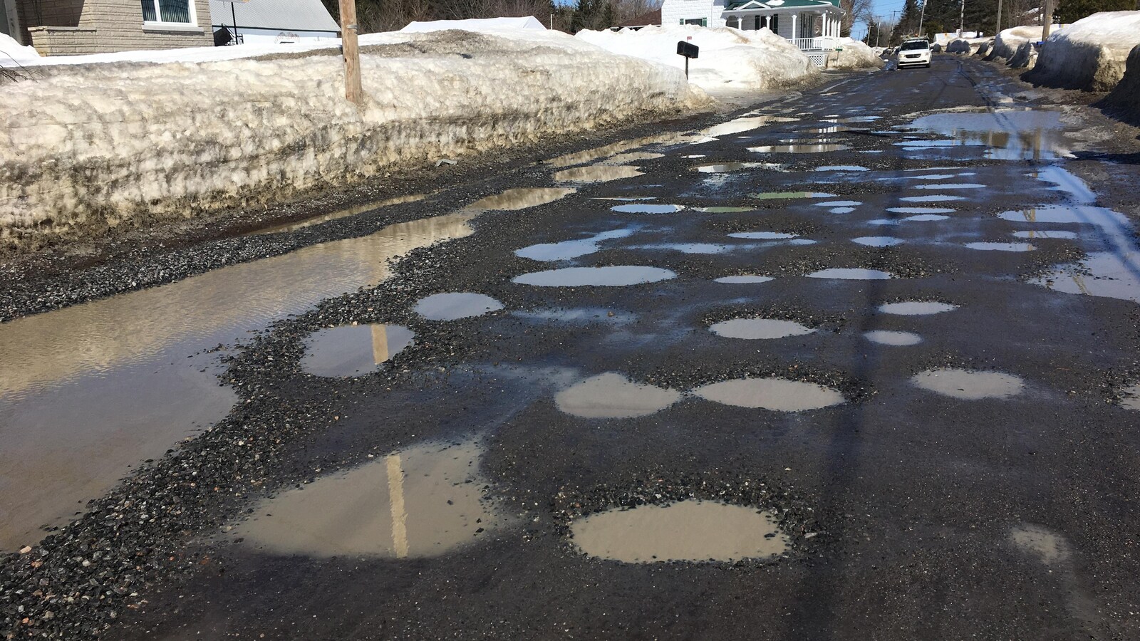 Une route de gravier est remplie de trous d'eau