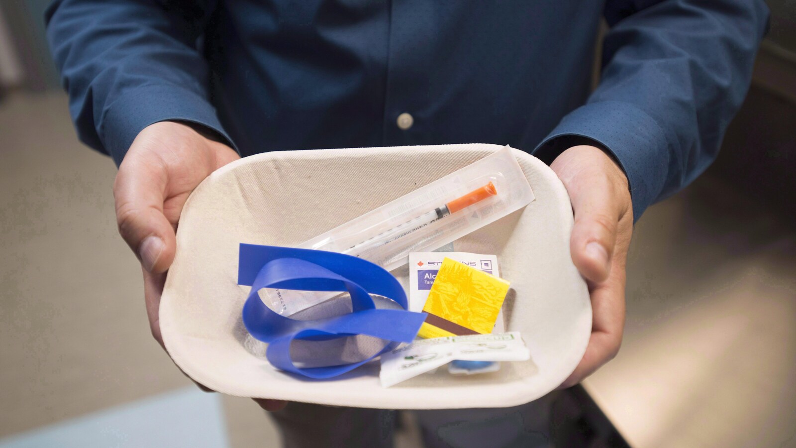 Un homme montre une trousse d'injection. Elle comprend une seringue, un ruban élastique et des compresses d'alcool.