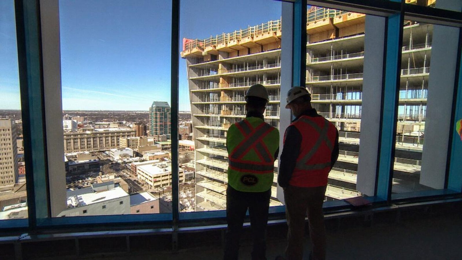 Deux hommes en vêtements de construction observent par la fenêtre le squelette d'un gratte-ciel.