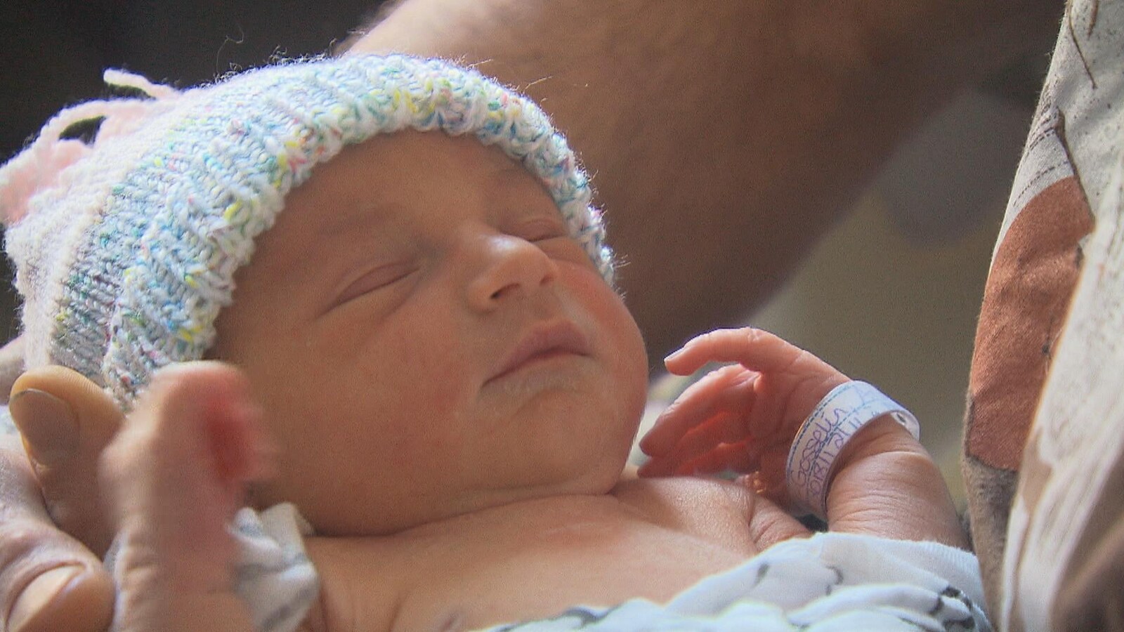 Un petit bébé d'à peine une journée a les yeux fermés et porte sur sa tête un petit bonnet de laine multicolore.