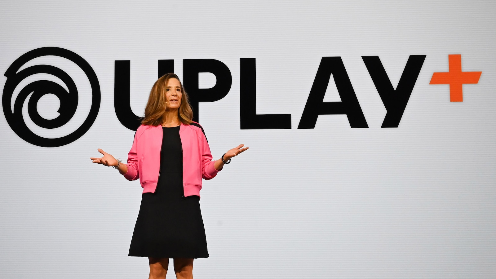 Une femme sur scène devant un écran géant affichant le logo du service Uplay+.