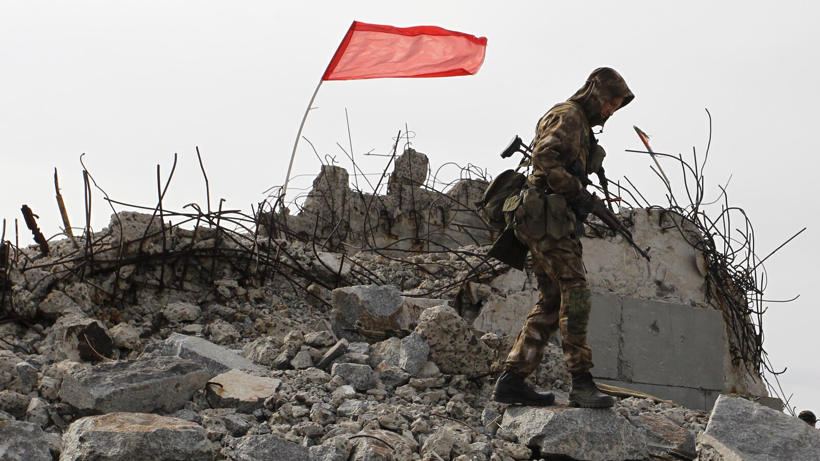 Un soldat monte la garde sur les ruines d'un bâtiment où flotte un drapeau.