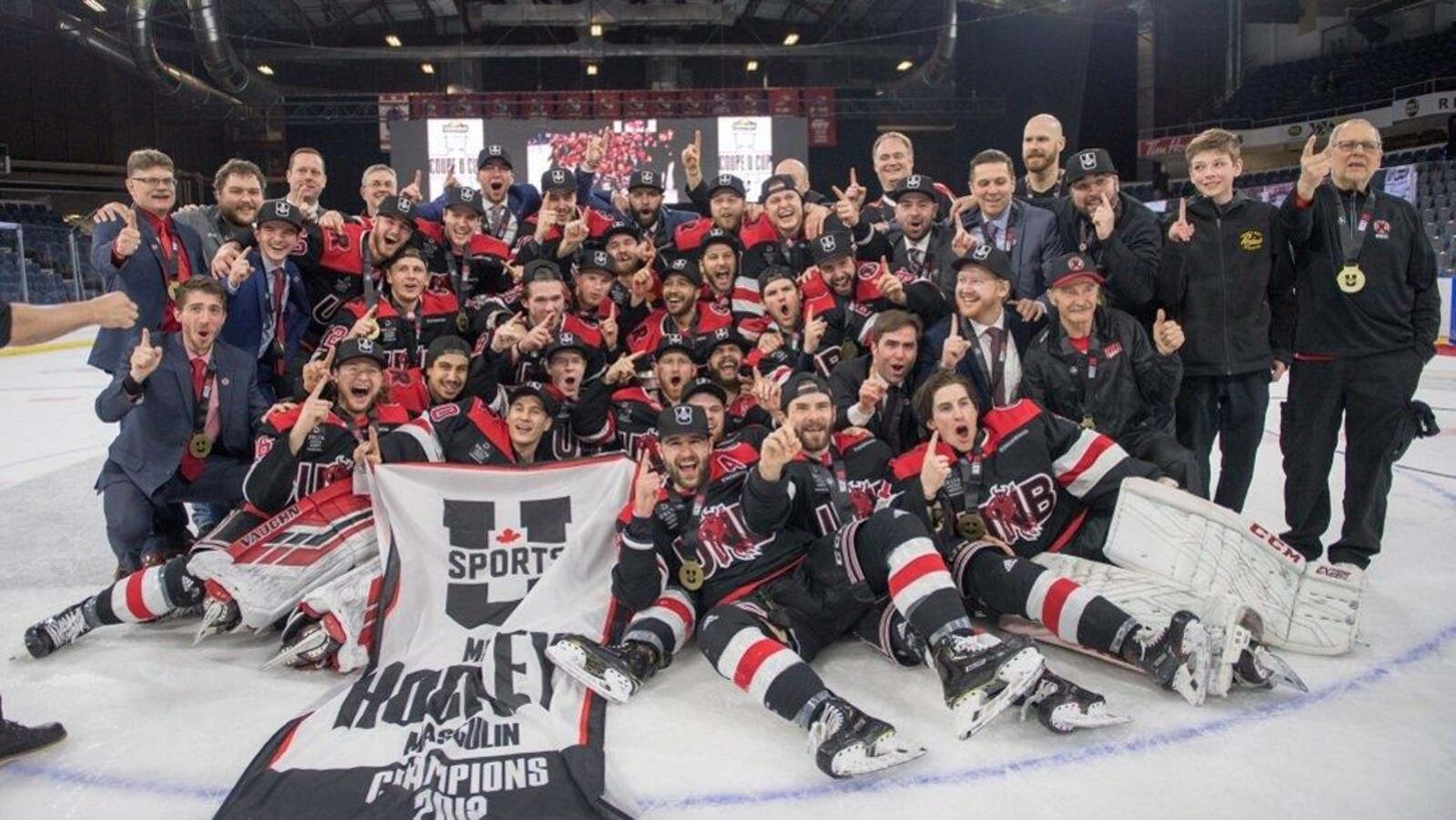 Tous les membres de l'équipe néo-brunswickoise rassemblés sur la patinoire font des signes de victoire.