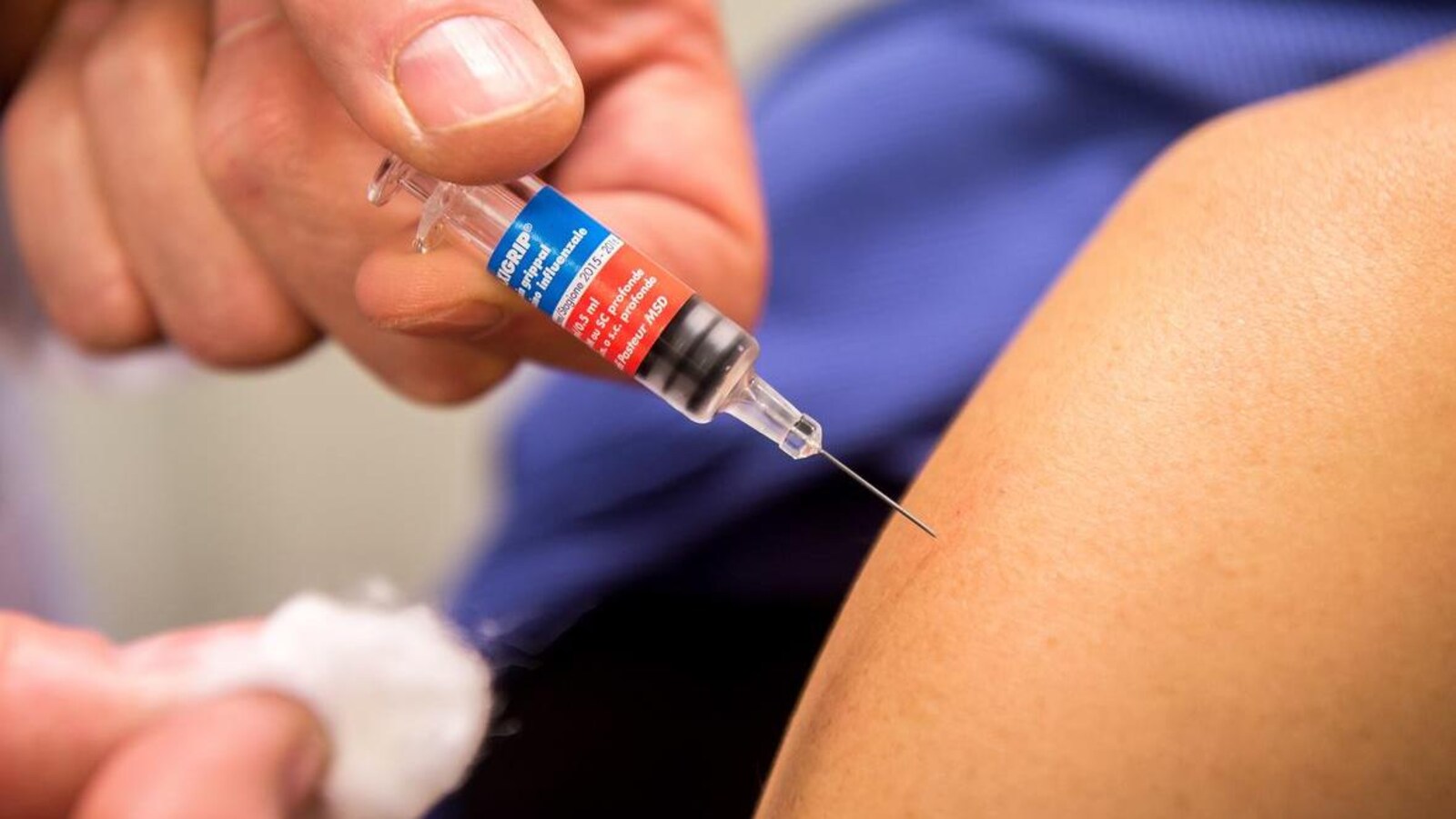 Acte de vaccination vu de près : des mains d'adulte maintiennent une petite seringue vidée, dont l'aiguille est plantée dans une épaule nue, et un petit morceau de coton.