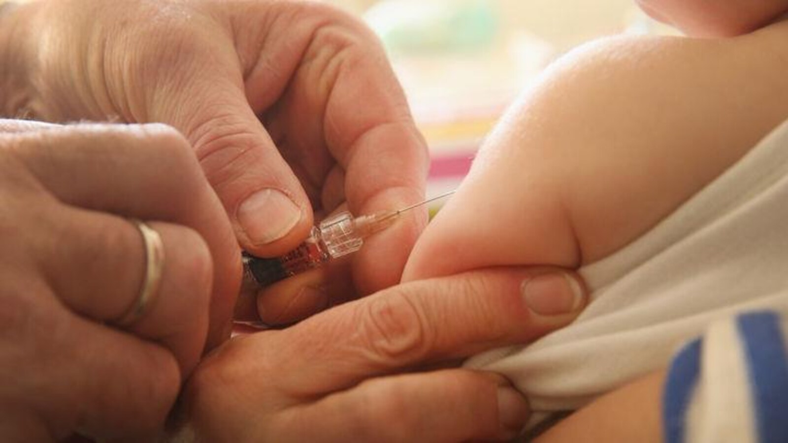 Une aiguille tenue par des mains d'adultes sur le bras d'un bébé