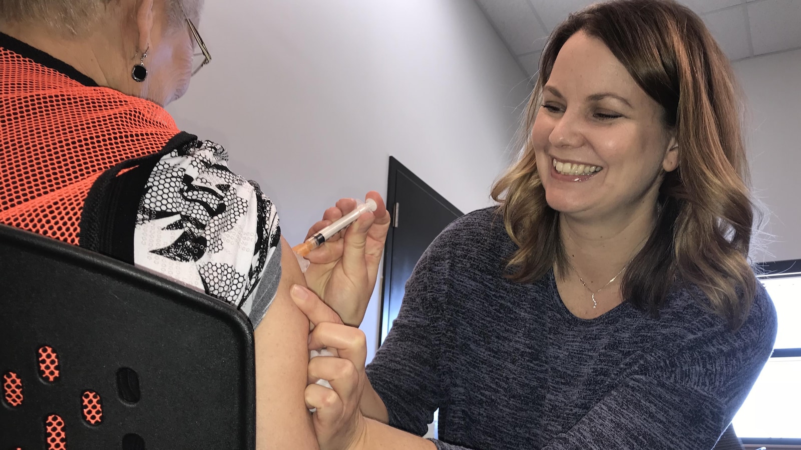 Une dame donne un vaccin à une autre dame, qu'on voit de dos.