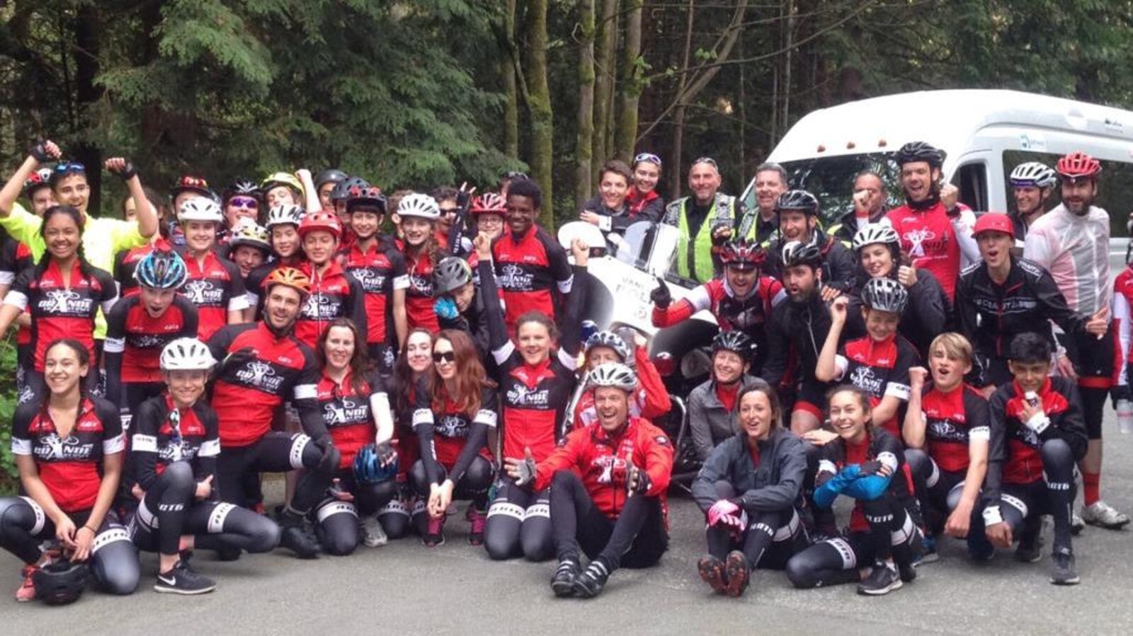 Un groupe d'une cinquantaine de jeunes en vêtement de cyclisme et une dizaine d'adultes posent devant une forêt.
