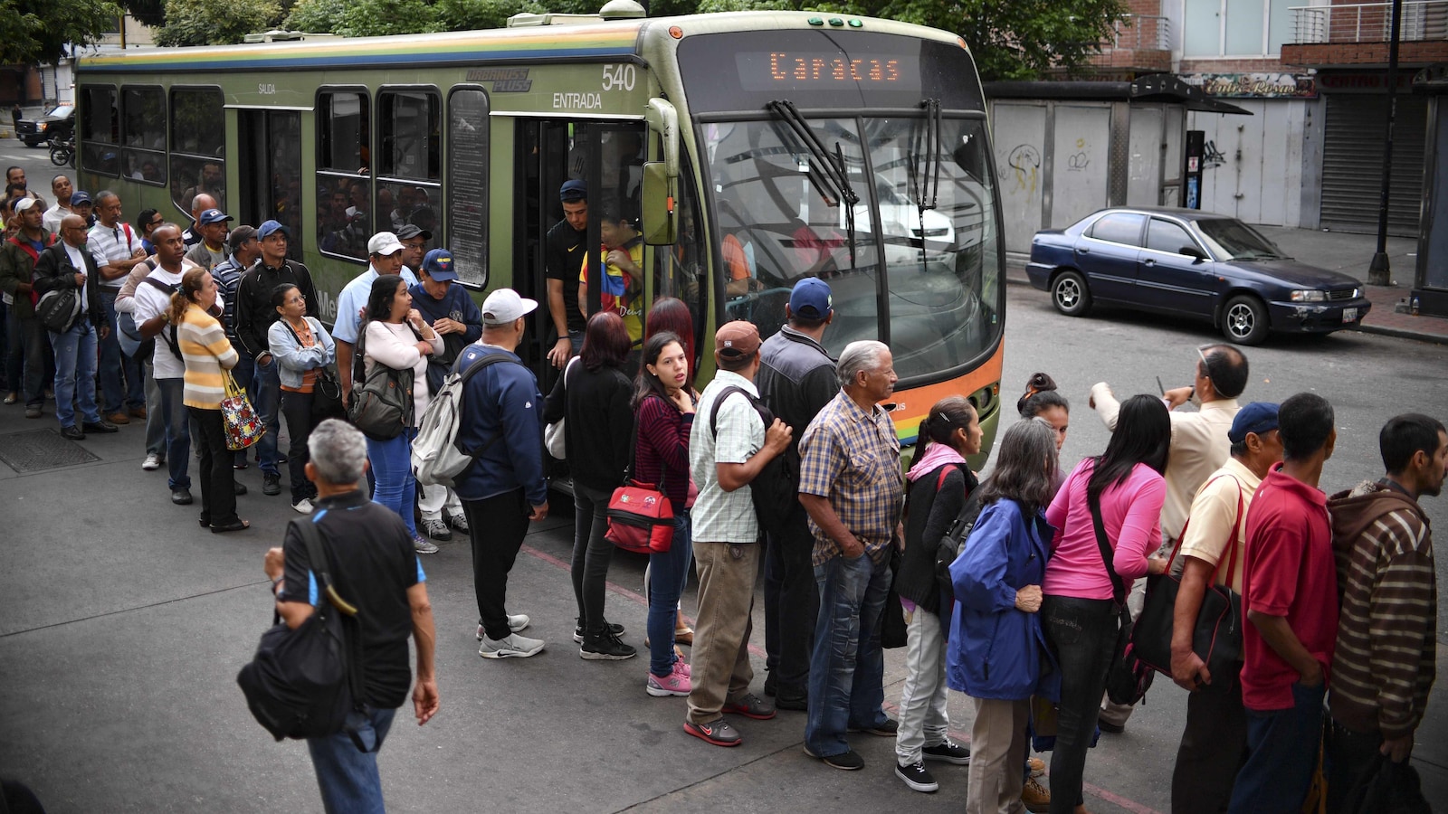Des dizaines de personnes sont debout l'une derrière l'autre sur le trottoir d'une rue de Caracas à côté d'un seul autobus.