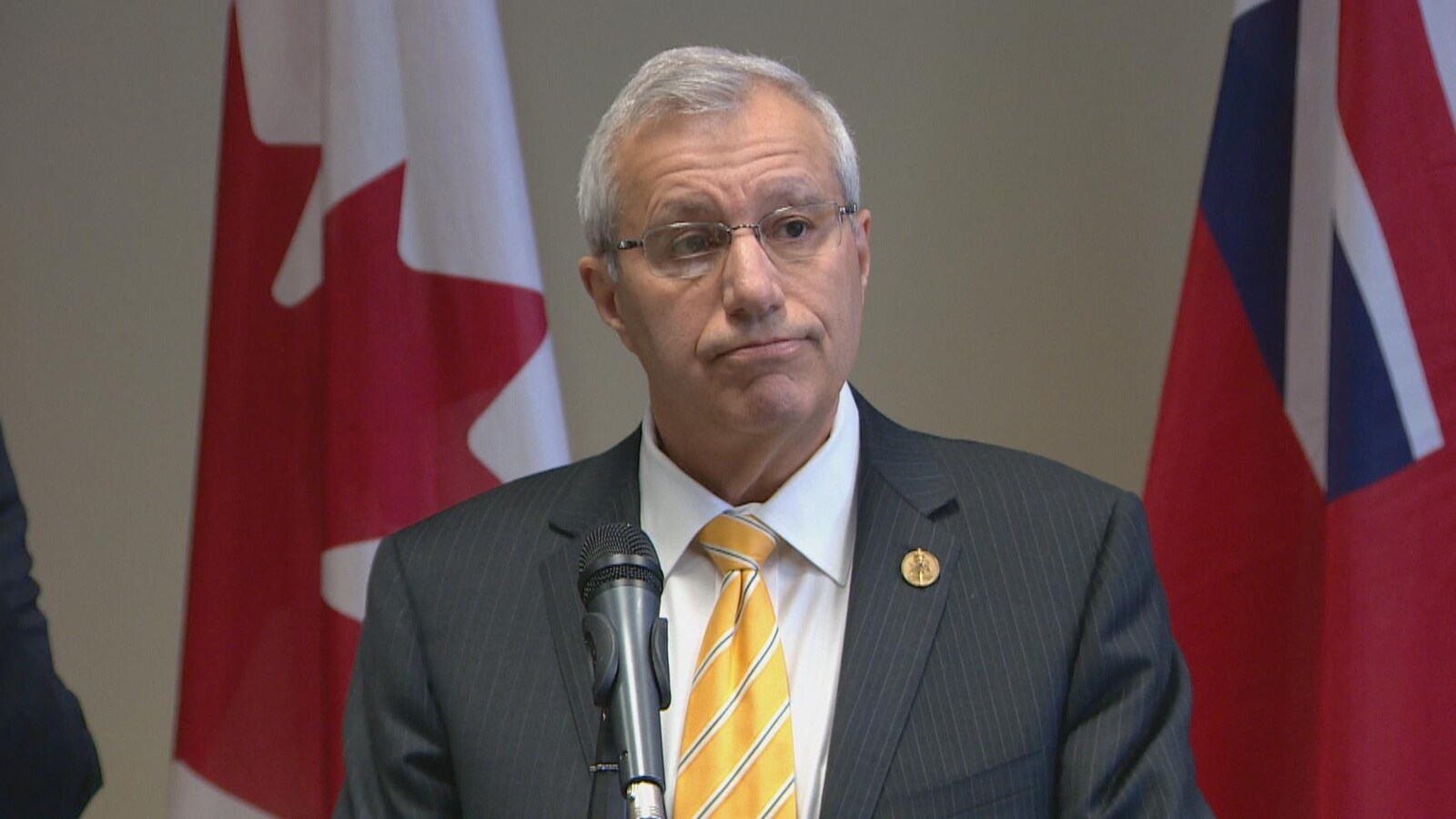 Photo de Vic Fedeli portant un complet gris et une cravate jaune devant un micro