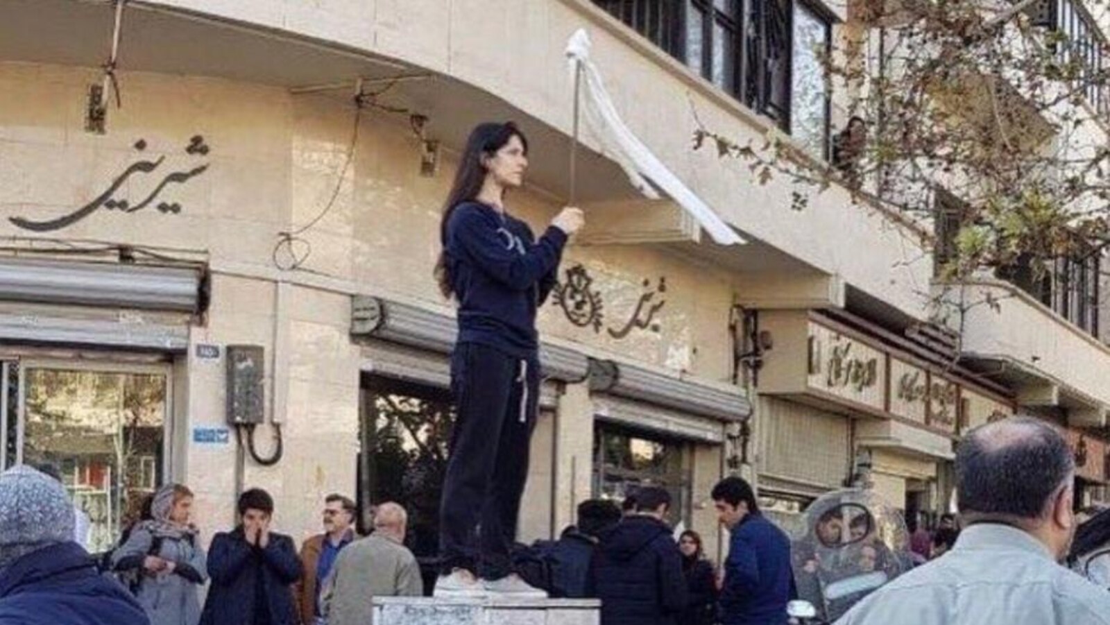 Une Iranienne, tête nue, brandit un bâton au bout duquel flotte son voile.
