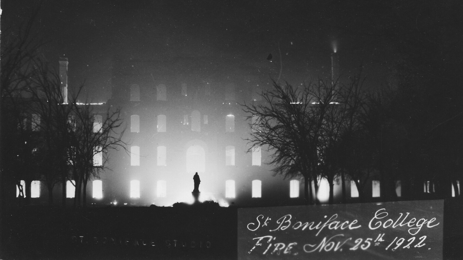 La façade en briques de l'ancien Collège de Saint-Boniface, illuminée par les braises. Une statue fantomatique semble planer devant l'édifice déformé.