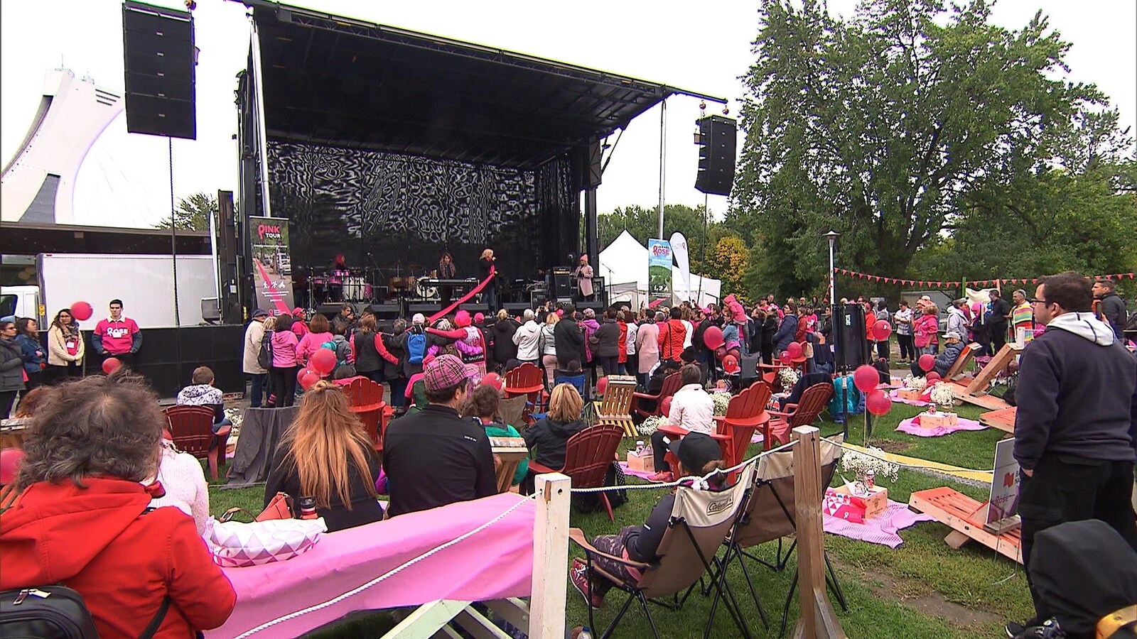 Des gens sont amassés devant une scène extérieure pour regarder une prestation musicale.