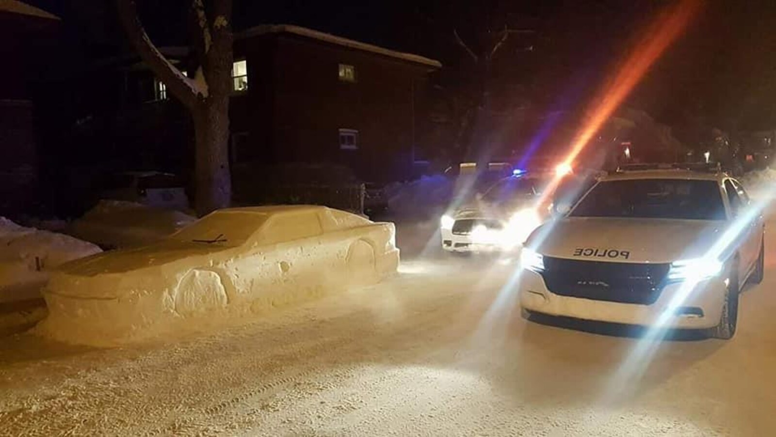 Deux voitures de police encadrent une voiture sculptée dans la neige.