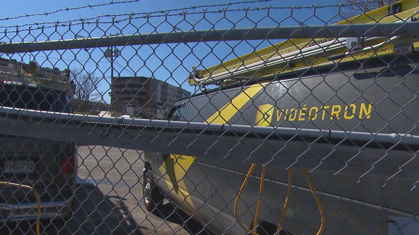 Des camions de Vidéotron sont stationnés derrière une clôture.