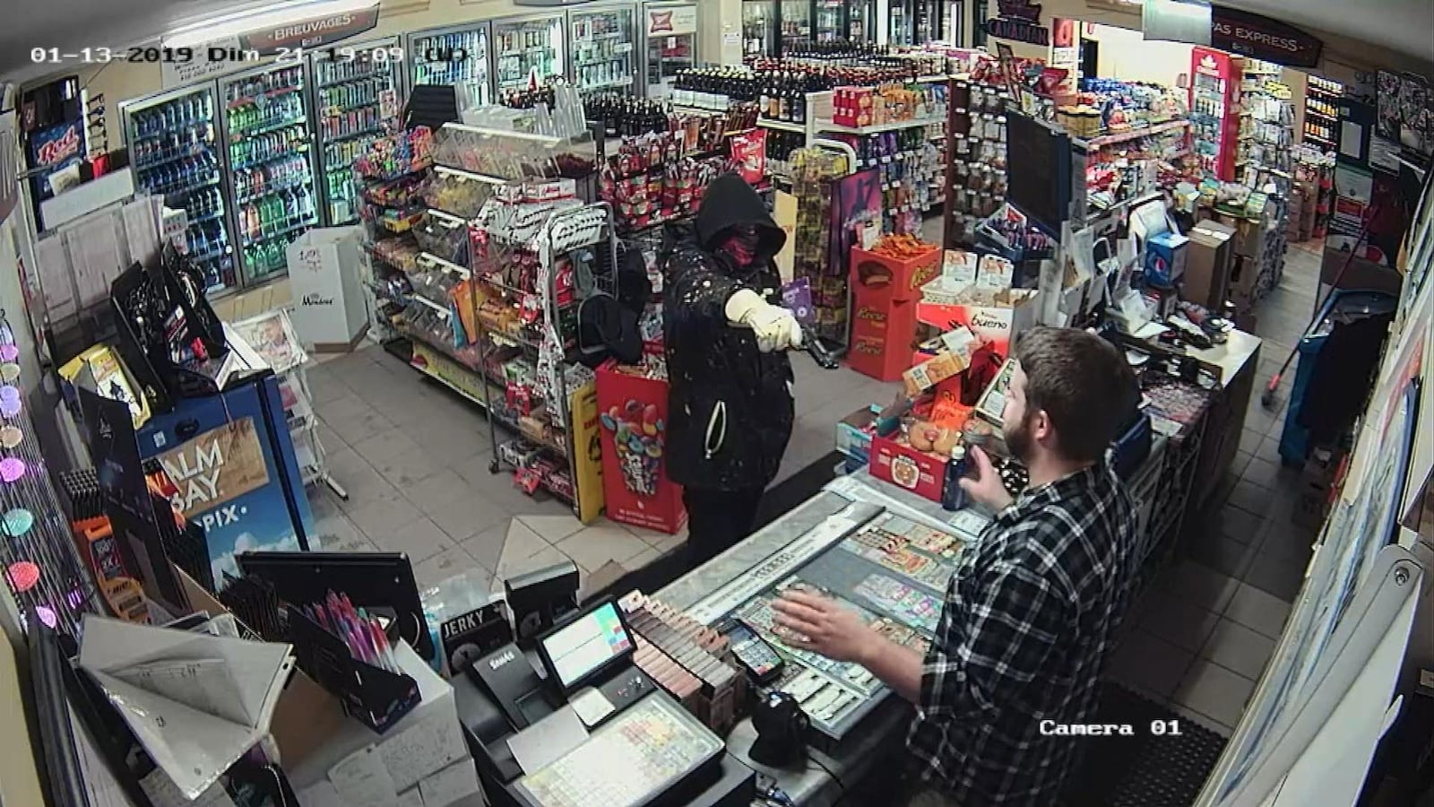 Dans un dépanneur, un homme cagoulé dans un dépanneur pointe une arme à feu en direction.
