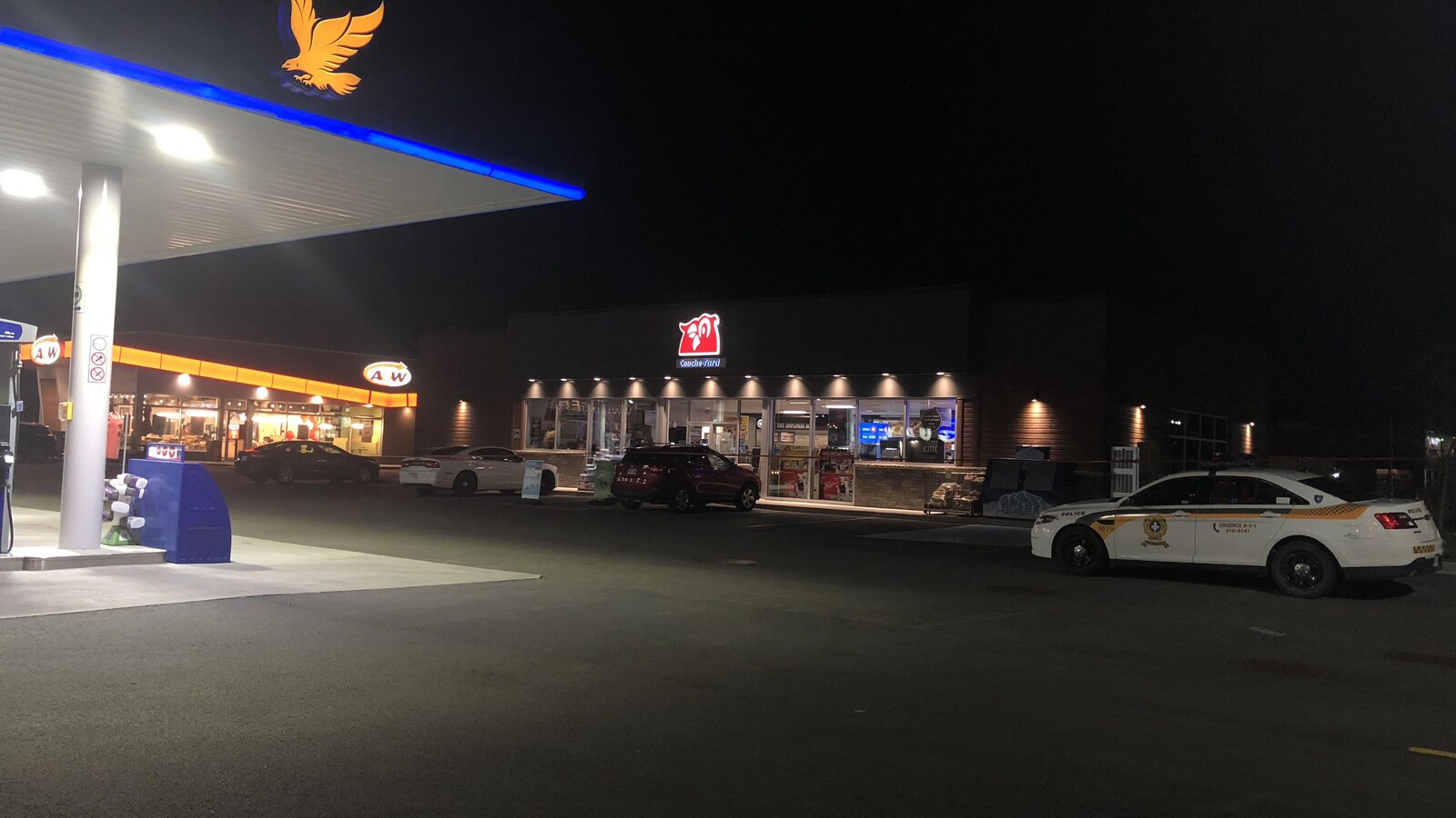 Une voiture de police est stationnée devant un dépanneur, la nuit.