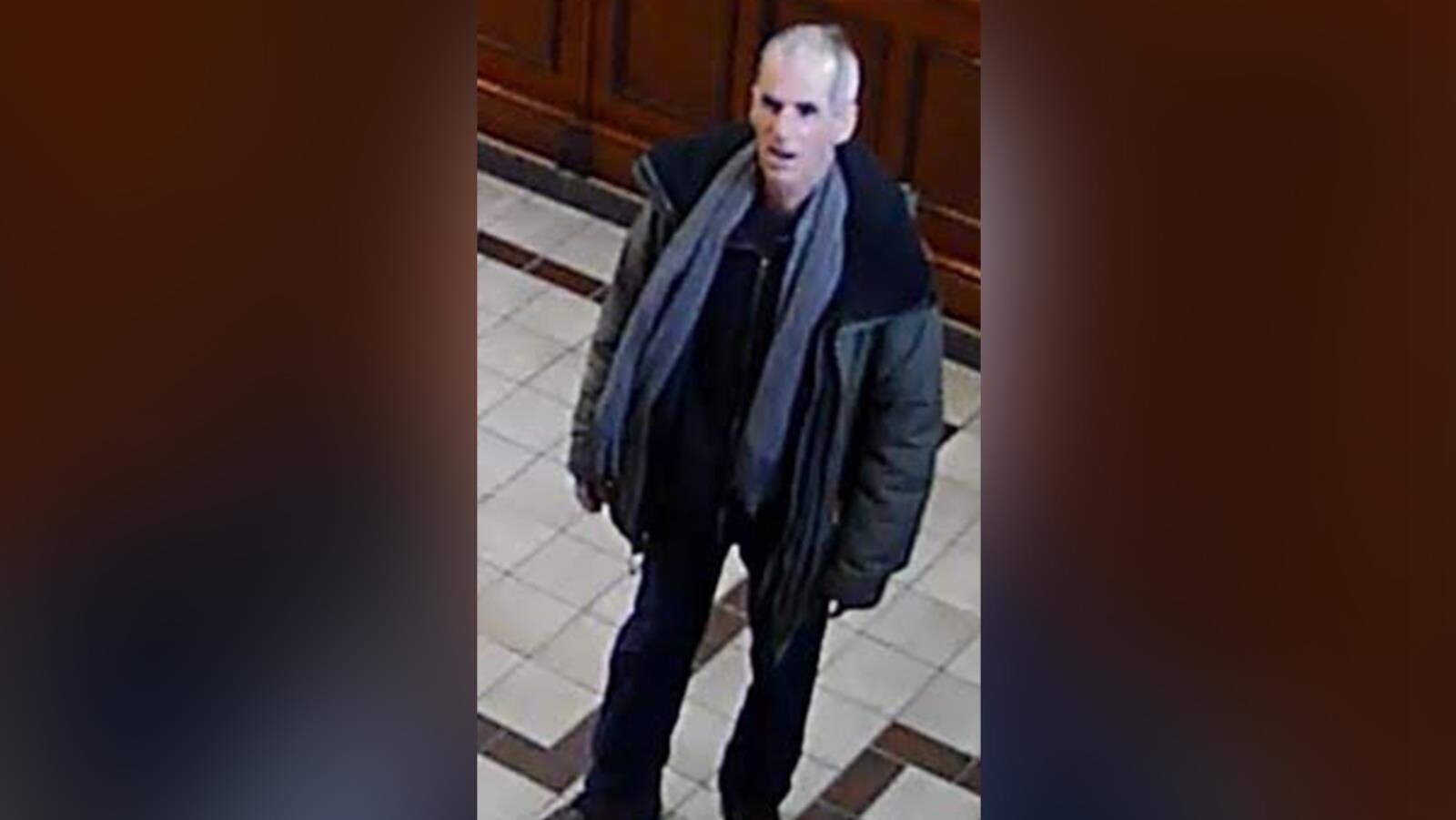 Le suspect portant un foulard gris, des pantalons noirs et un manteau vert.