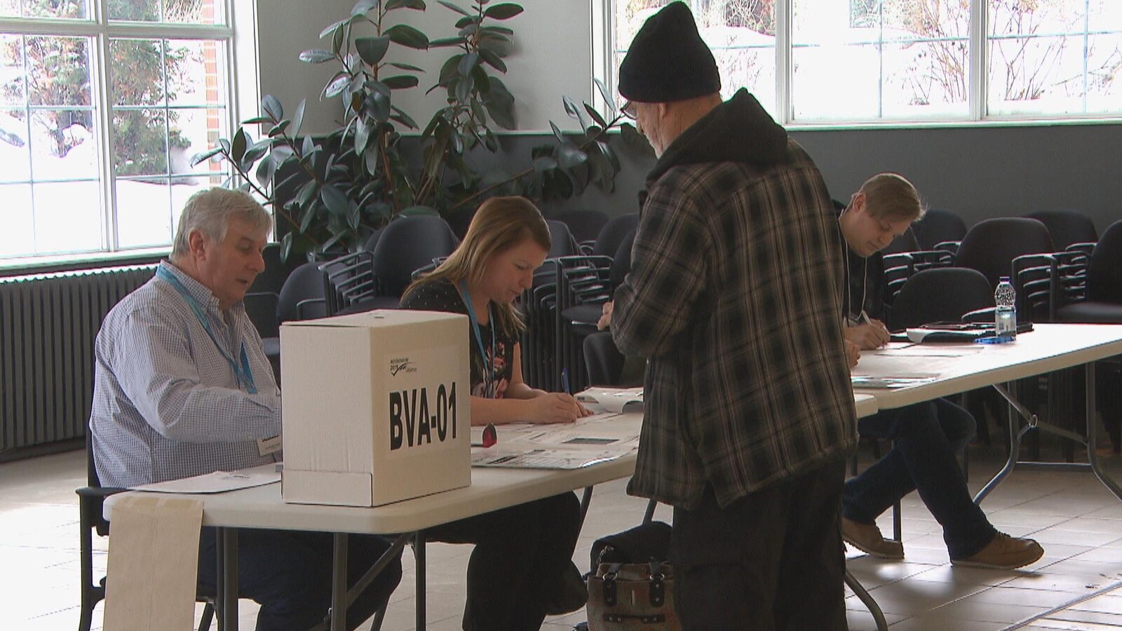 Un homme s'inscrit pour voter. Il y a un homme et une femme qui lui parlent.