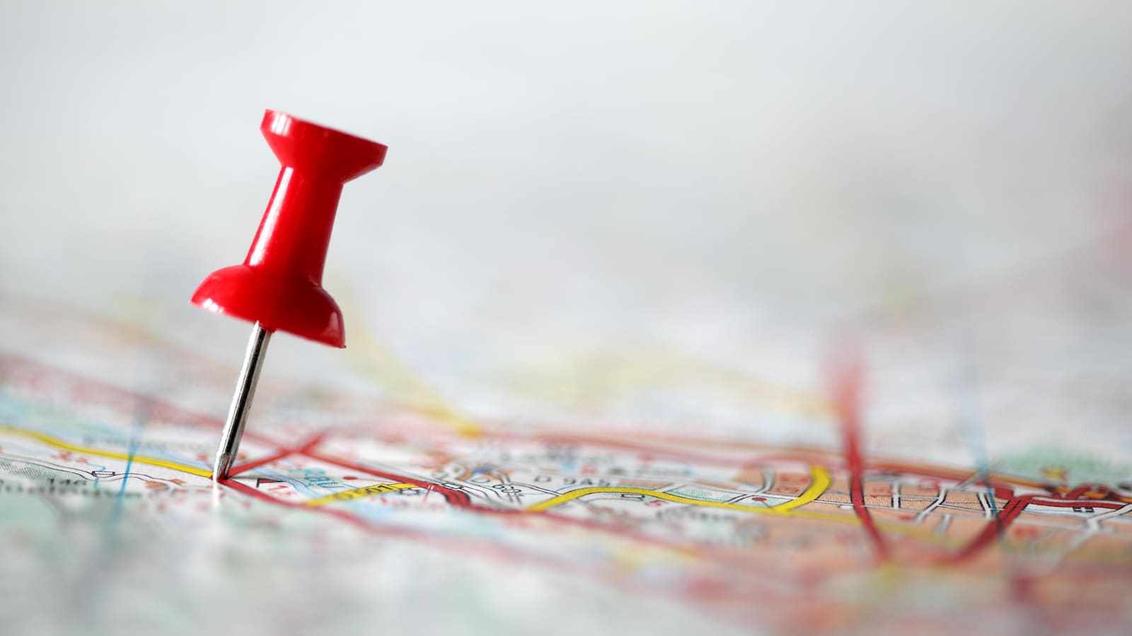 Une punaise rouge sur une carte routière floutée.