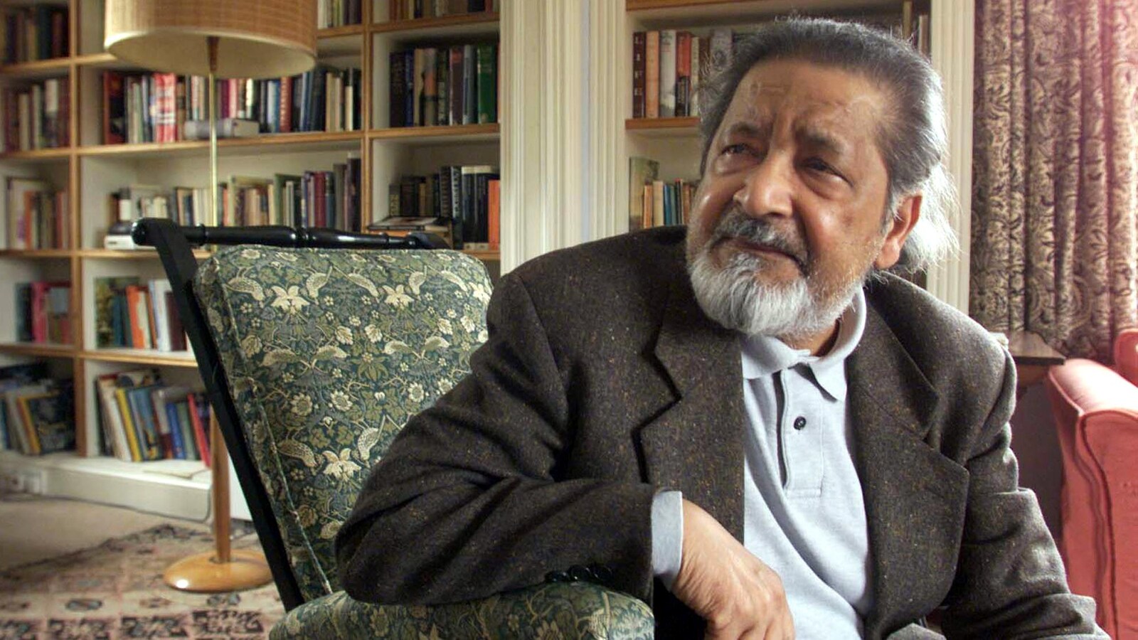 L'auteur britannique V.S. Naipaul, assis sur une chaise dans une bibliothèque.