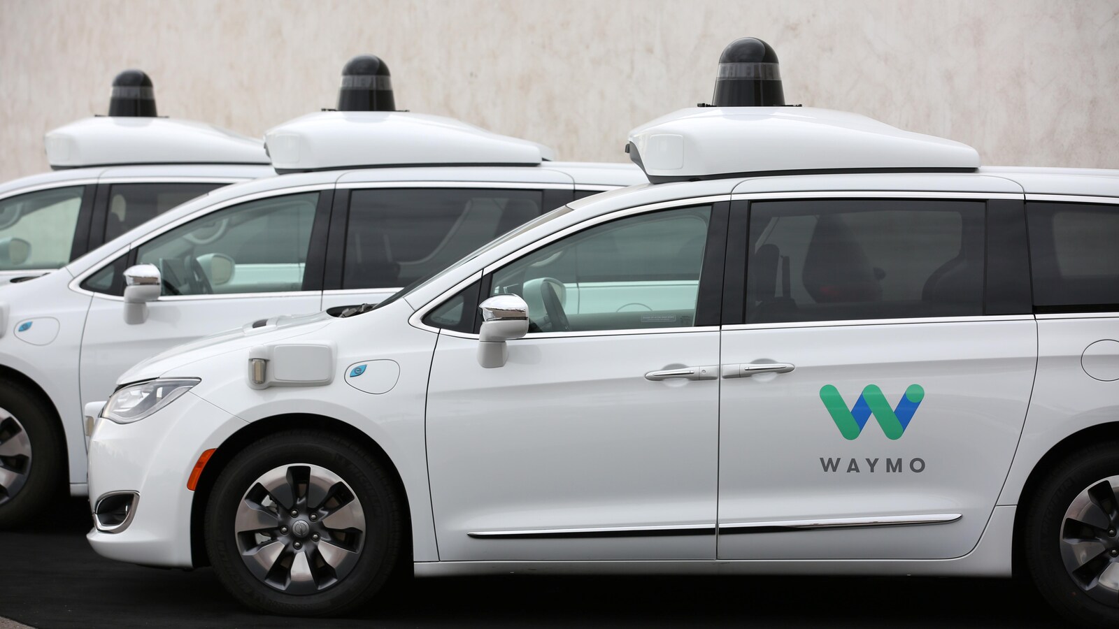 Une photo montrant trois mini fourgonnettes blanches portant le logo de Waymo sur l'une de leurs portes.