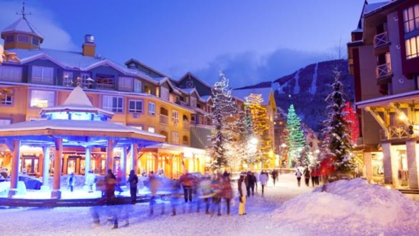 Des passants se promènent dans une rue enneigée et illuminée de Whistler à la nuit tombante.