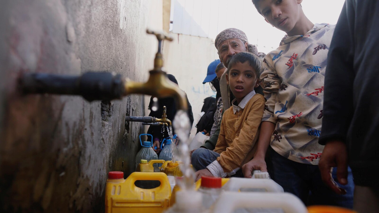 Adultes et enfants remplissent des bouteilles d'eau à des robinets installés à l'extérieur d'un bâtiment.