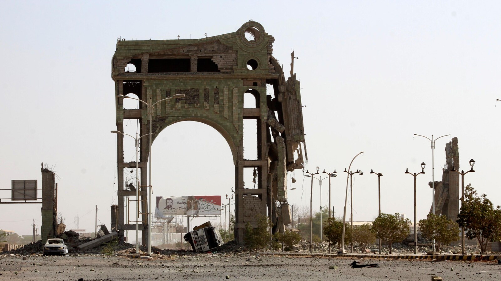 Une arche en briques est partiellement en ruines, entourée de voitures et de lampadaires détruits dans une ville du Yémen.