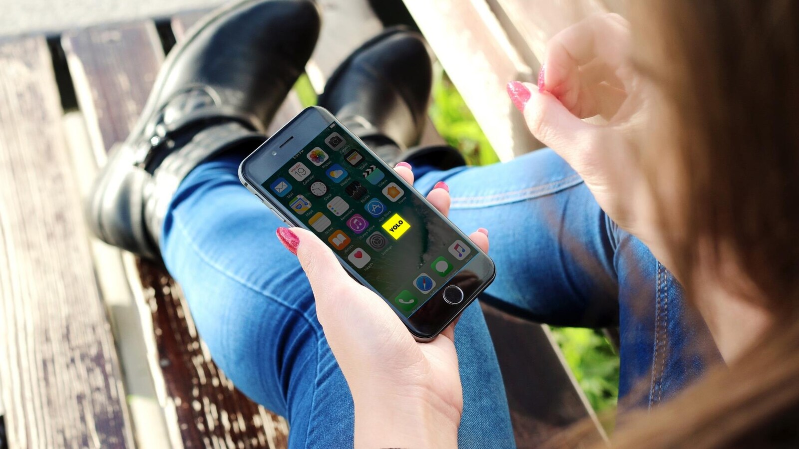 Une jeune femme assise sur un banc de parc consulte son téléphone cellulaire.