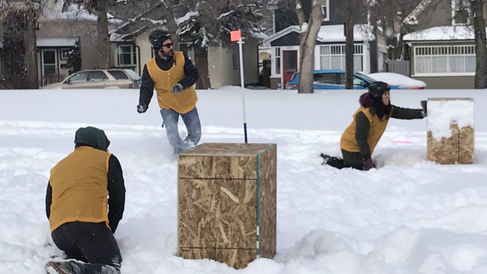Deux joueurs de yukigassen se cachent derrière des boîtes pendant qu'un autre s'apprête à lancer une boule de neige.