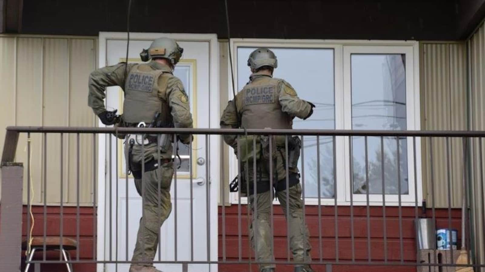 Deux policiers en uniformes de combat sont sur un balcon devant la porte d'un appartement.