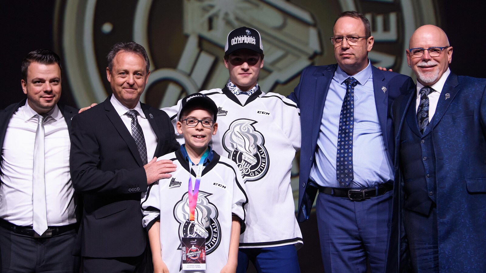 Un jeune joueur de hockey vêtu de son chandail pose fièrement après avoir été repêché dans la LHJMQ.