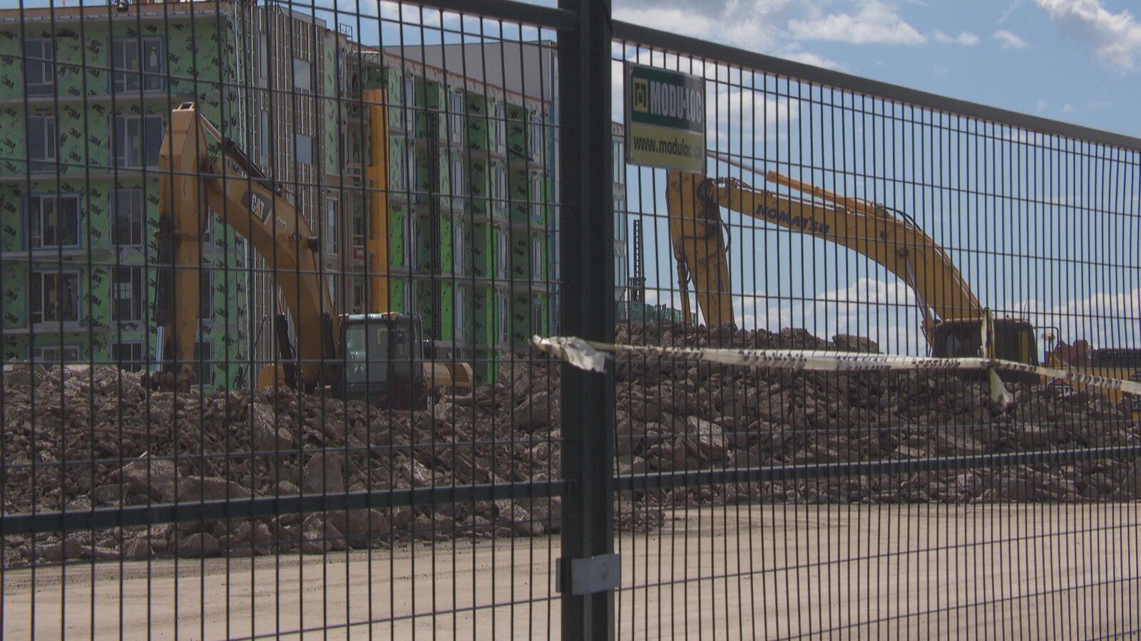 Deux grues s'affairent à retirer des roches et du sol autour de l'immeuble en construction.