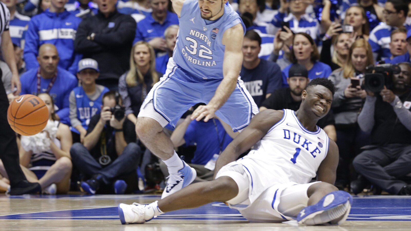 Un joueur de basketball assis au sol grimace de douleur, son soulier de sport visiblement fendu du talon aux orteils.