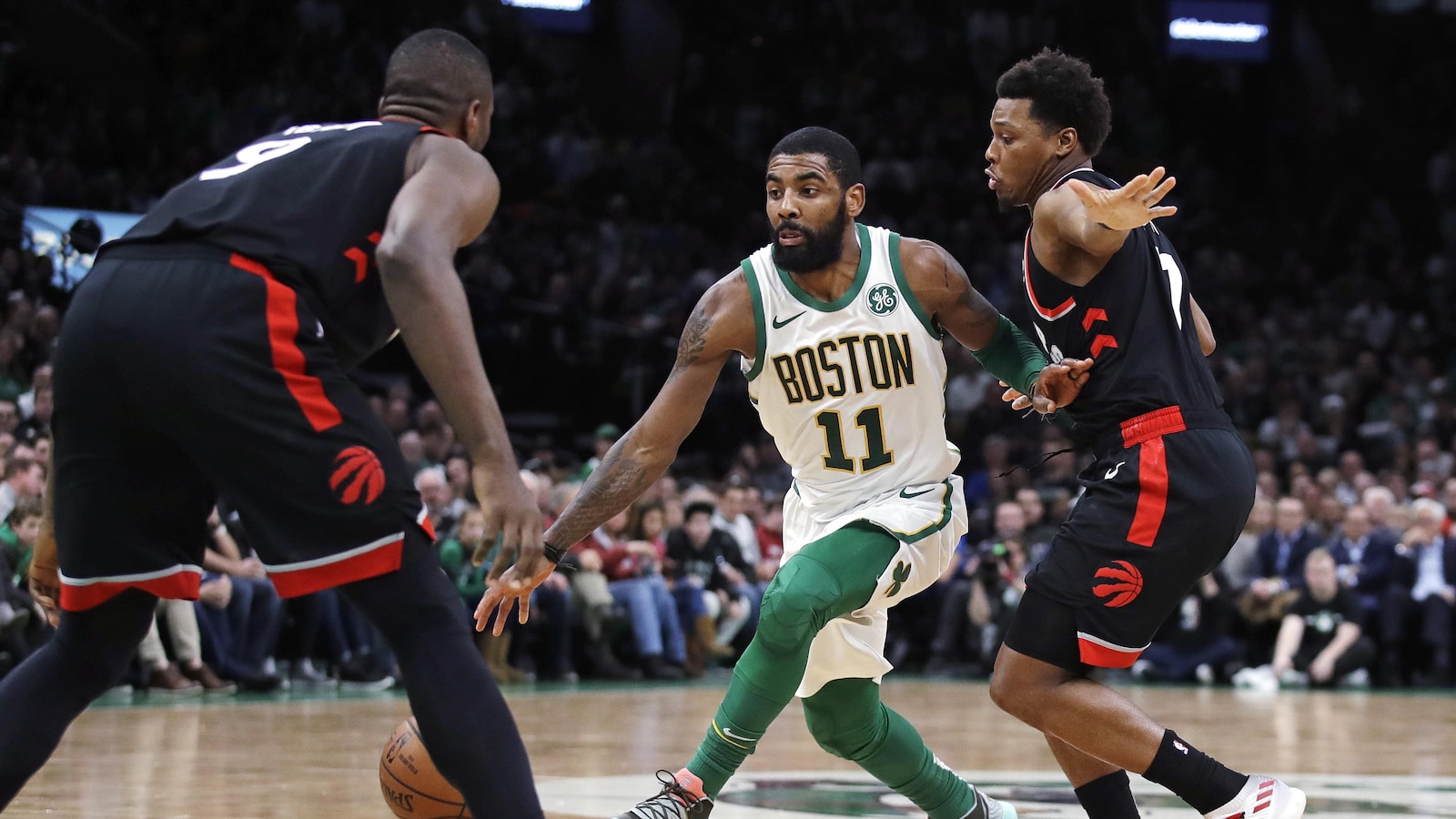 Kyrie Irving (au centre), des Celtics de Boston, tente d'accéder au panier entre Serge Ibaka (à gauche) et Kyle Lowry, des Raptors de Toronto.
