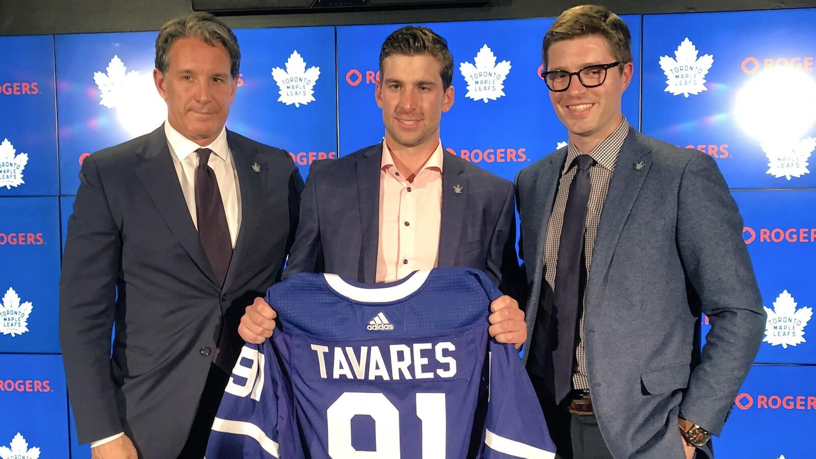 Entouré de Brendan Shanahan et Kyle Dubas, John Tavares tient dans ses mains un chandail des Maple Leafs de Toronto.