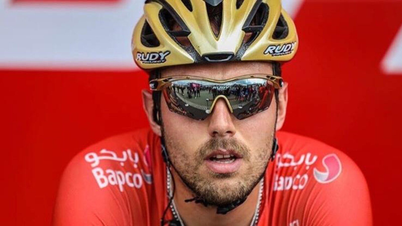 Gros plan sur le visage de Sonny Colbrelli, lunettes de soleil et casque dorée sur la tête.