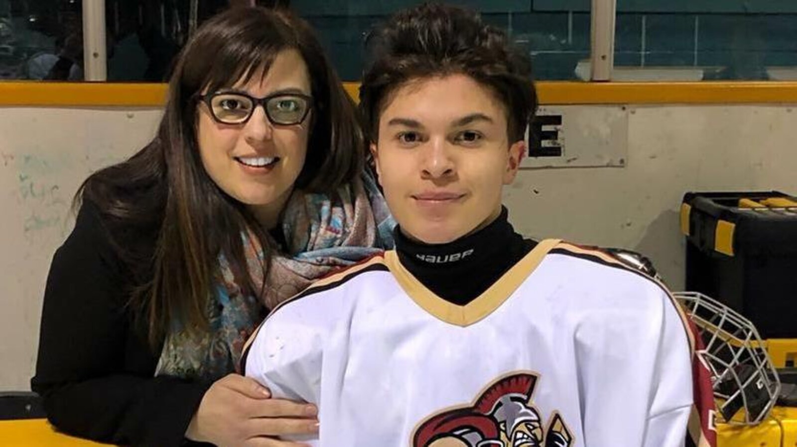 Un jeune homme en habit d'hockey sur une patinoire pose avec sa mère.