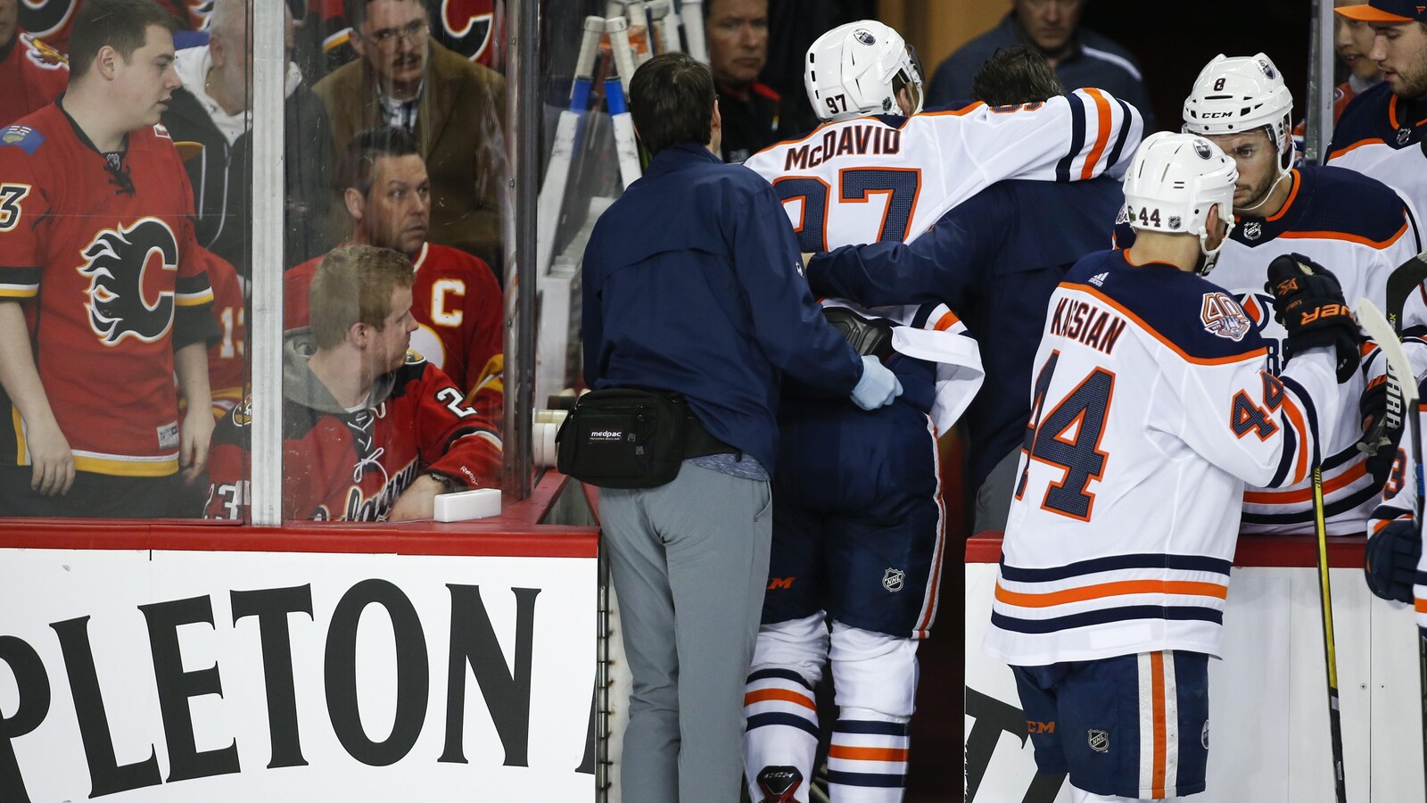 Connor McDavid est supporté par deux membres de l'organisation des Oilers alors qu'il quitte la patinoire.