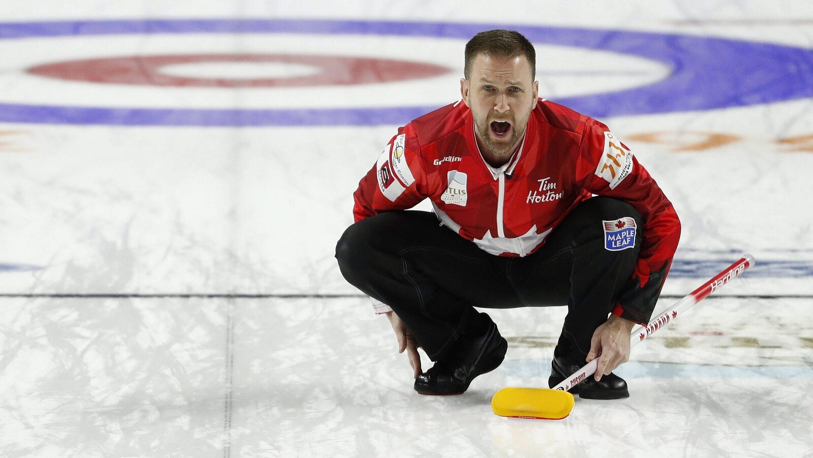 Brad Gushue, accroupi sur la glace, crie ses directives.