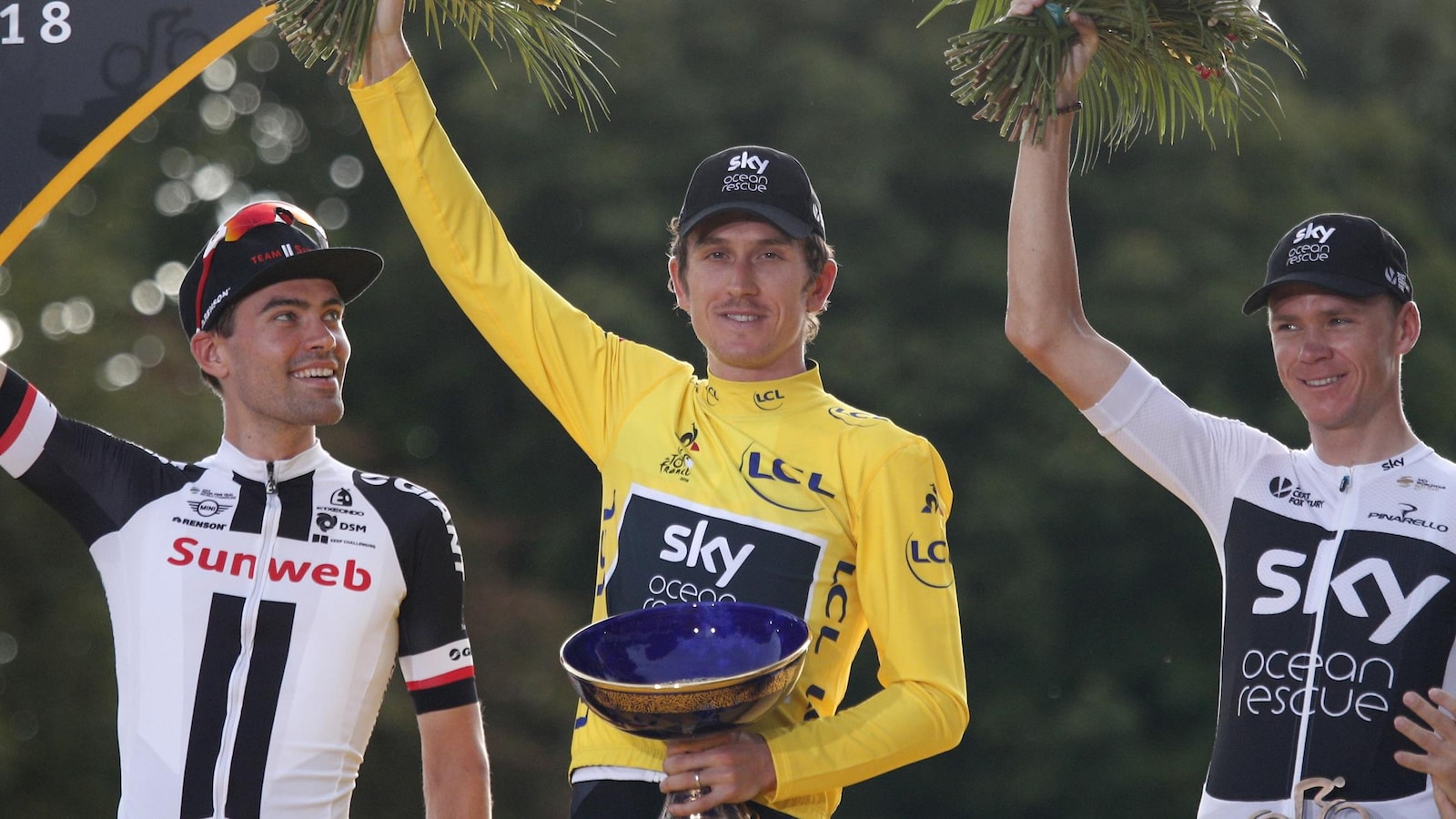 Il tient le trophée de la main gauche et des fleurs dans la droite.