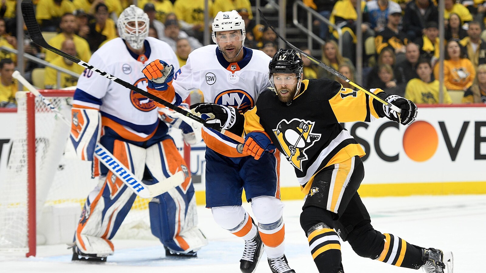 Johnny Boychuk surveille son adversaire des Penguins, Bryan Rust. On voit le gardien Robin Lehner en arrière-plan, devant le filet de son équipe.
