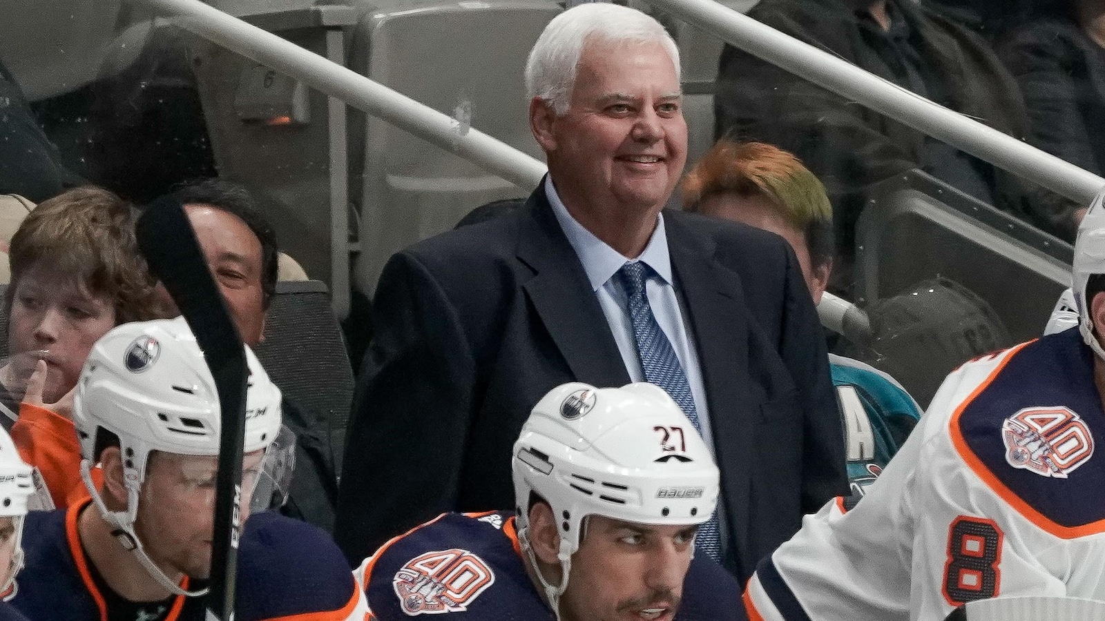 Ken Hitchcock affiche un grand sourire alors qu'il se tient derrière le banc des Oilers durant un match.
