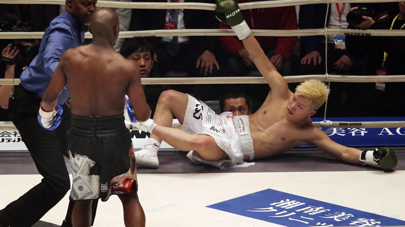 Le Japonais Tenshin Nasukawa tente de se relever à l'aide des câbles après avoir été envoyé au tapis par Floyd Mayweather.