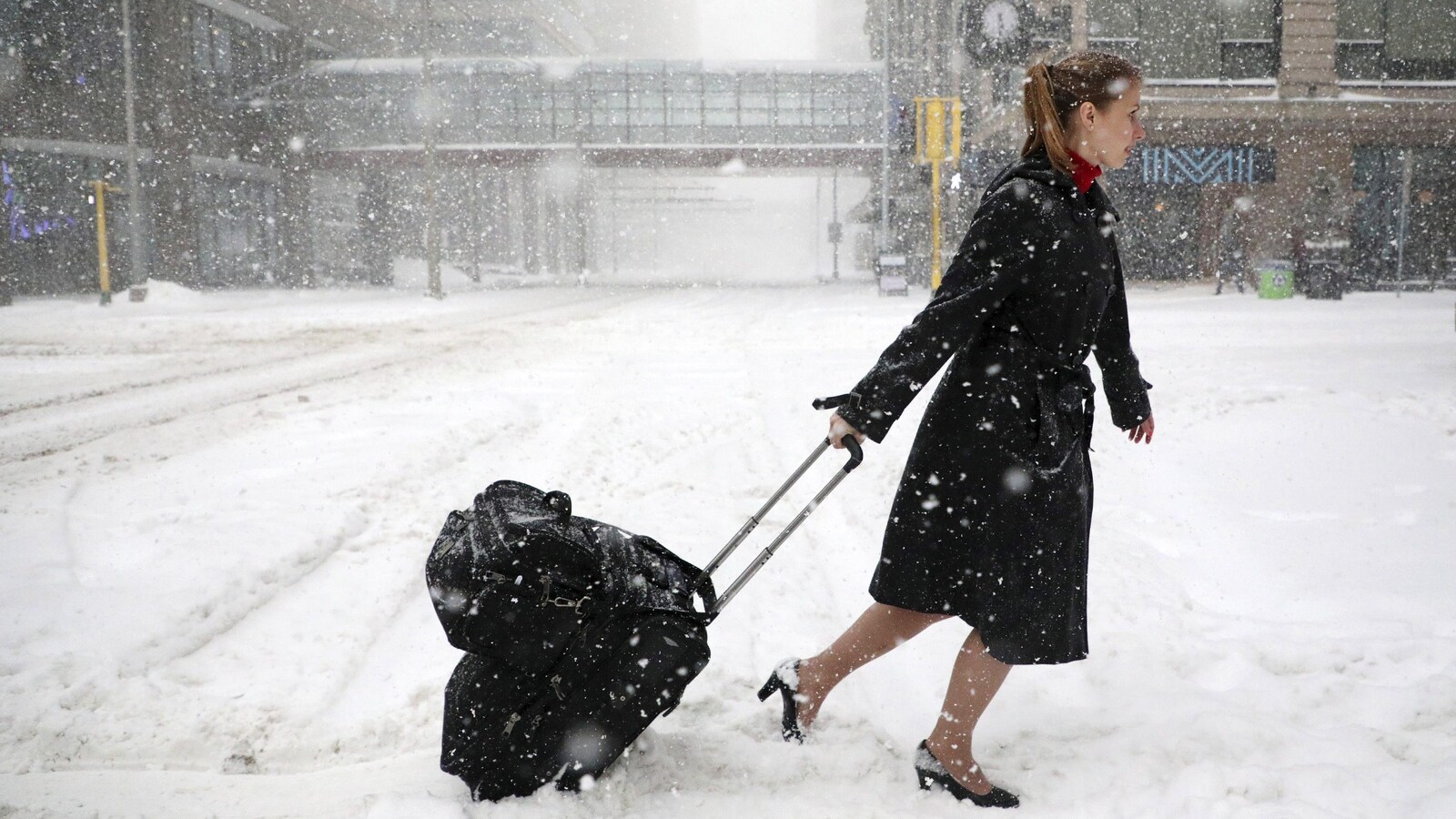 Une agente de bord traverse une rue de Minneapolis en tirant sa valise sous une neige abondante.